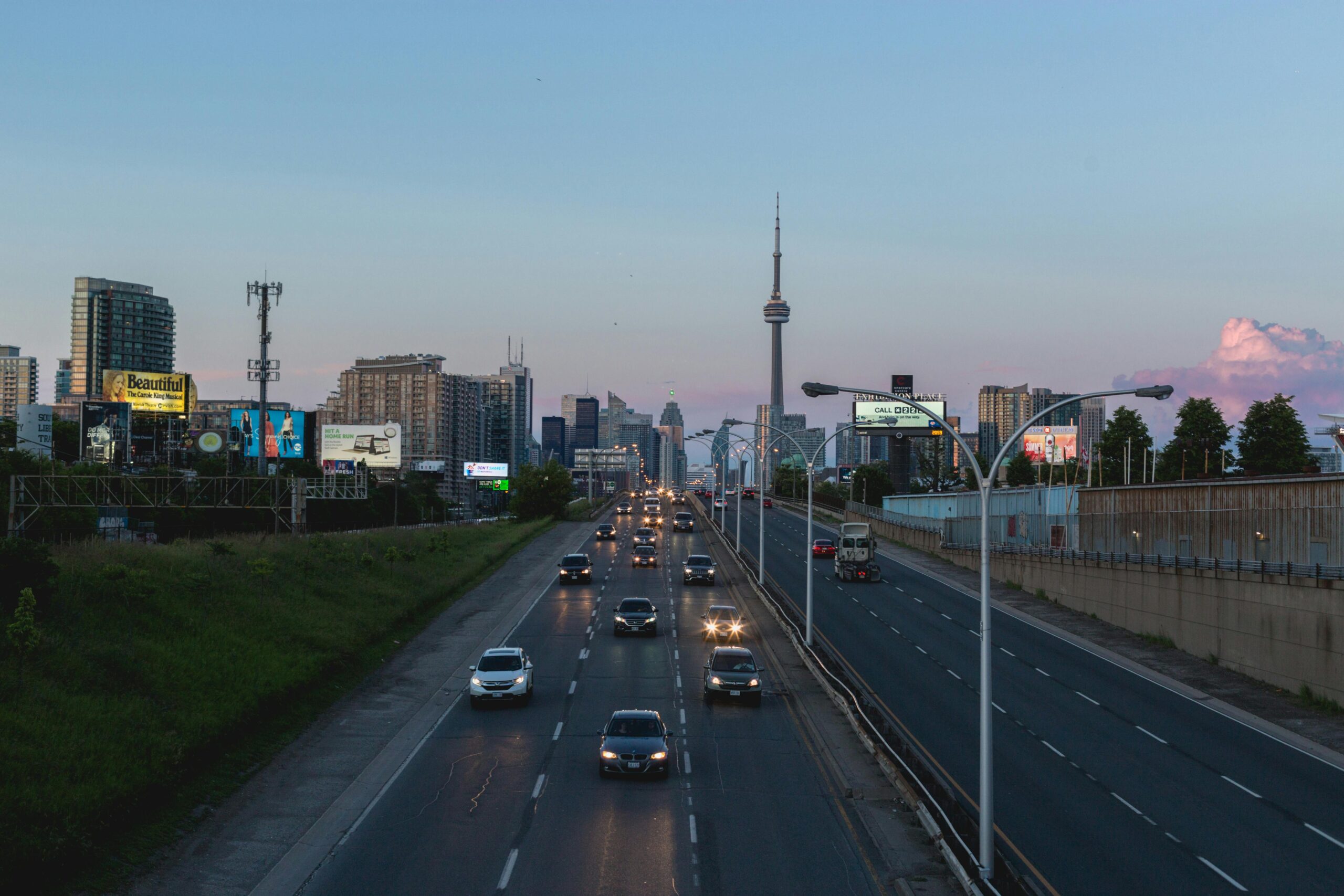 View of Toronto skyline at sunset with CN Tower, expressway, and traffic.